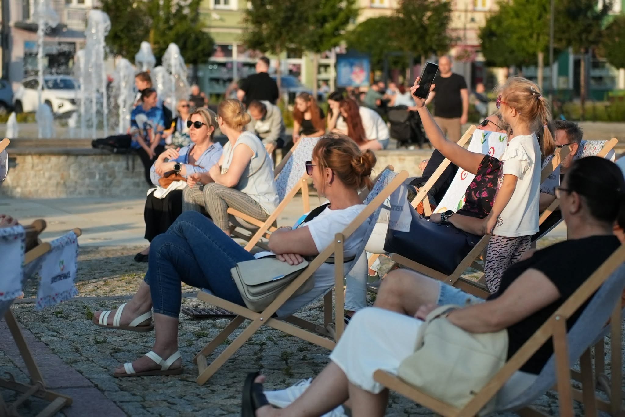 Publiczność siedząca na leżakach przy fontannie na rynku